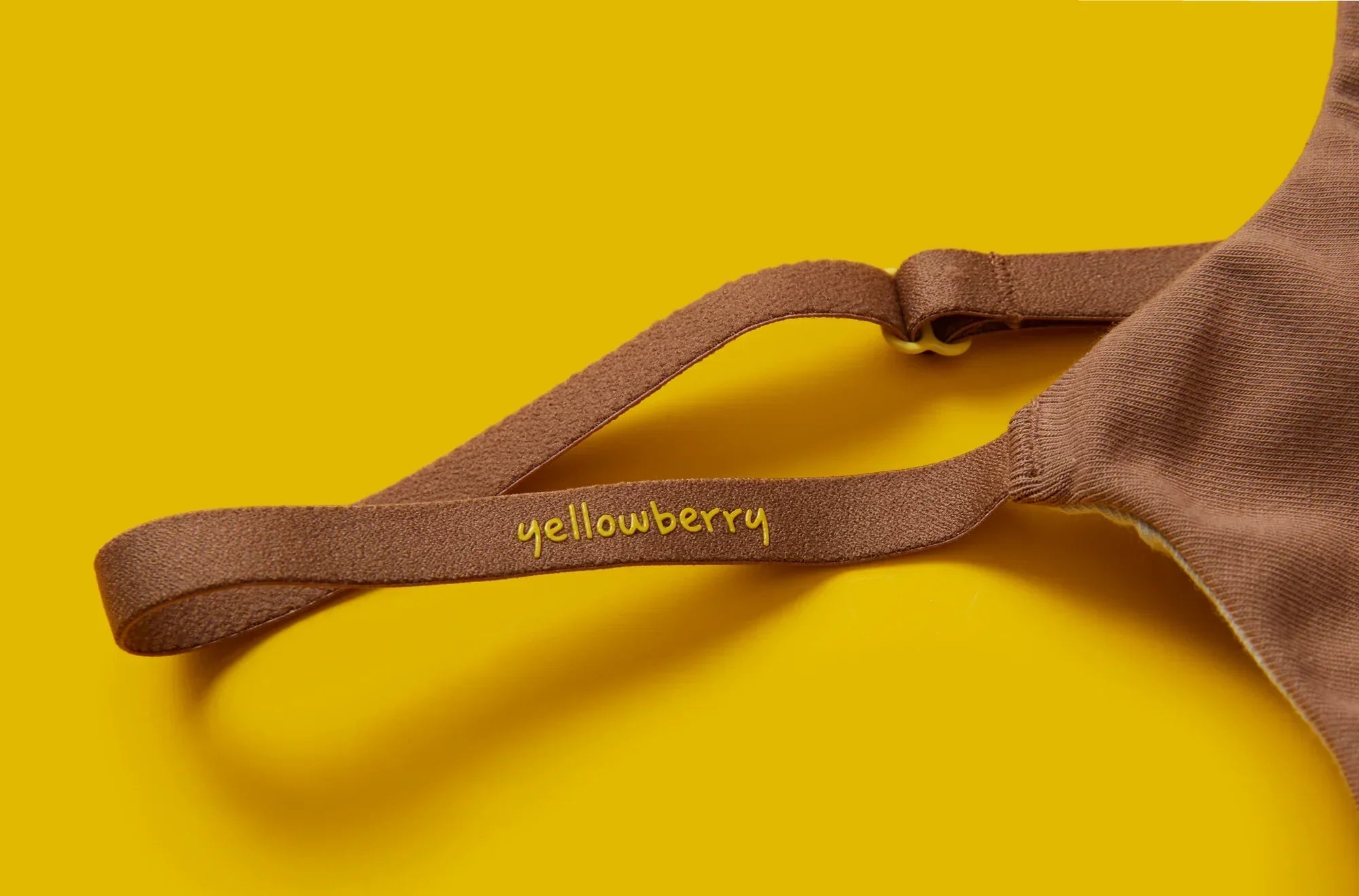 Close up of a strap of a Yellowberry Pipit Mocha Bra on a yellow background